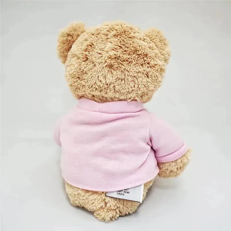 Brown teddy bear wearing a pink shirt, viewed from the back, with a small label visible near the bottom.