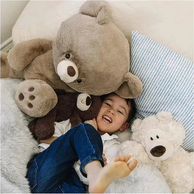 A child happily cuddles with multiple plush bears, including a large beige Philbin plush toy, on a cozy surface.