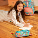Colorful pencil pouch with floral design rests on the floor as a girl writes in a notebook, surrounded by colored pencils.