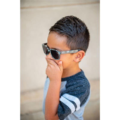 Child wearing Stephen Joseph Axolotl sunglasses, covering mouth with hand, showing playful expression.