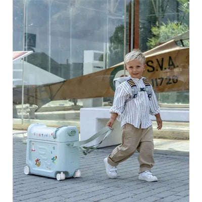 A young child in a striped shirt and beige pants is pulling a light blue Stokke Jetkids Travel Bundle with stickers attached.
