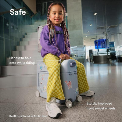 Child seated on Stokke Jetkids Bedbox in Sea Green, showcasing sturdy wheels and a handle for riding, in an airport setting.