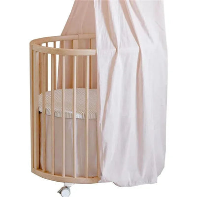 Stokke Sleepi Mini Bed Skirt by Pehr in blush, featured on a circular crib with a striped mattress.