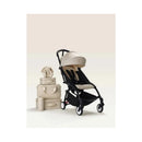 Stokke Yoyo³ 6+ stroller with a black frame, beige seat fabric, and matching Bonpoint bundle leg rest, alongside storage bags and a plush toy.