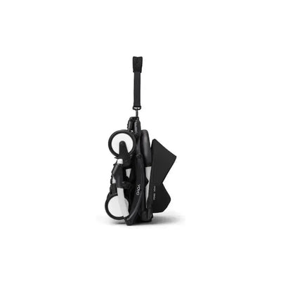 Stokke Yoyo³ stroller in black, compactly folded with a carrying strap, featuring sleek design and white accents.