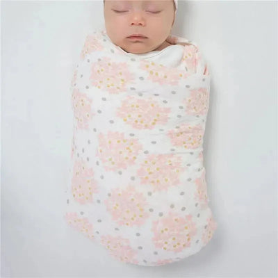 Muslin swaddle blanket featuring a floral design with gold shimmer, wrapping an infant peacefully sleeping.