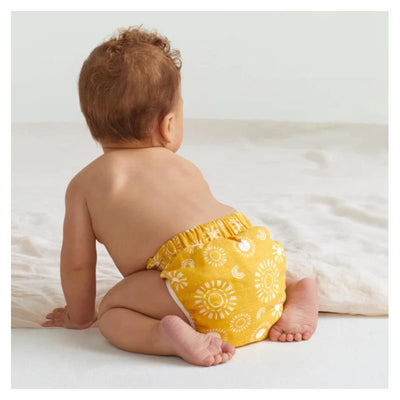 Baby crawling on a soft surface wearing a yellow Swaddle Designs reusable cloth diaper cover with a sun pattern.