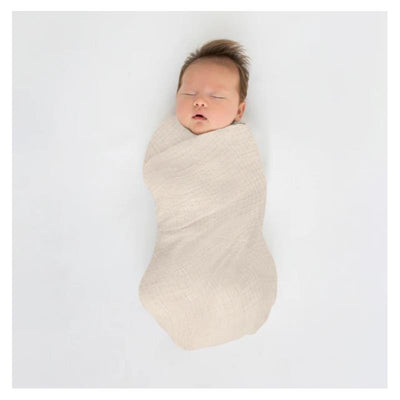 Oatmeal muslin swaddle blanket wraps a sleeping baby, showcasing its soft texture and light color against a white background.