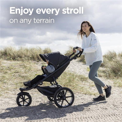 Single child all-terrain stroller in black with a canopy, being pushed on a sandy path by a woman dressed in activewear.