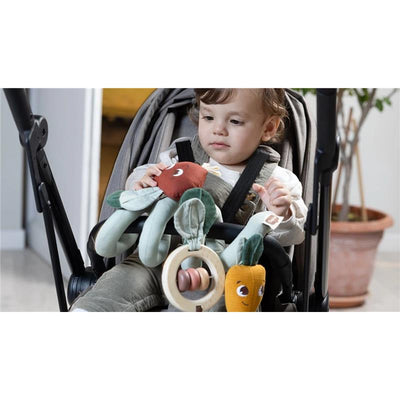 Child seated in a stroller, engaging with colorful soft toys from the Tiny Love Garden of Adventure collection.