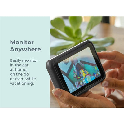 Baby monitor screen showing toys in a play area, held by a person, with a green plant in the background.