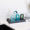 Boon LAWN drying rack displaying colorful cups and TWIG accessories on a countertop beside white dishware.
