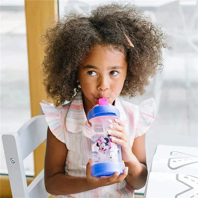 Girl sipping from a Tomy Disney Minnie Sip & See water bottle, featuring a pink top and Minnie Mouse design.