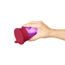 Boon SNUG Spout silicone sippy lid in pink attached to a transparent purple sippy cup, held by a hand.