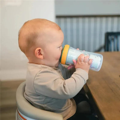 Toddler using a Tomy Bluey insulated sippy cup with a yellow lid while seated at a wooden table.