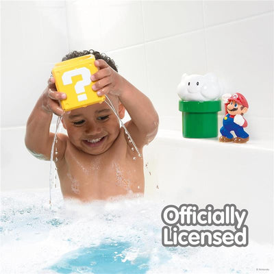 Child happily holds a yellow block pouring water while surrounded by bath toys, including Mario and a green pipe.
