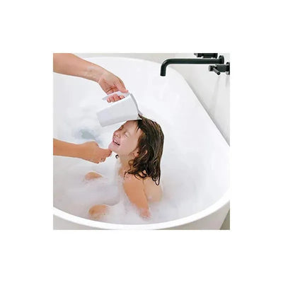 A small child smiles in a bathtub as a hand pours water over their head using the Ubbi Bath Rinse Cup.
