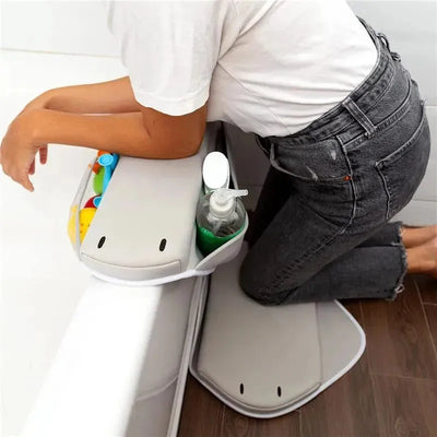 Cushioned gray elbow rest with compartments for bath toys and hand soap, used by a person kneeling next to a bathtub.