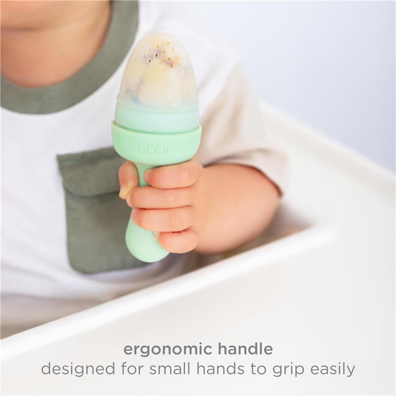 Baby holds an Ubbi Smoothie Purple Baby Food Feeder with an ergonomic handle, designed for easy gripping.