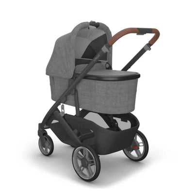 Uppababy Cruz V3 stroller in Charcoal Mélange with a carbon frame and saddle leather handle, featuring a removable bassinet.