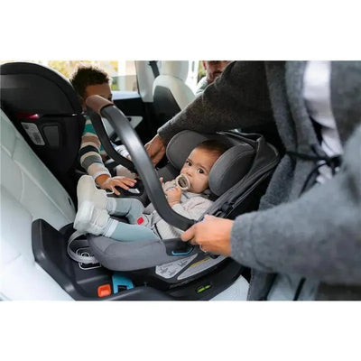 Extra Aria Car Seat Base installed in a vehicle with a baby seated and a caregiver adjusting the handle.