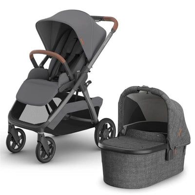 Uppababy Kona Stroller in graphite color with brown leatherette handlebar and a matching bassinet, both featuring a modern design.