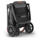 Uppababy Kona stroller in graphite color, featuring a sleek black seat and brown leatherette handle, folded for storage.