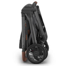 Uppababy Kona Stroller folded flat, showcasing its graphite color, with brown leatherette handle and details.