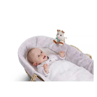 Smiling baby in a crib reaching for a Vulli Baby Sophie Plush toy, a soft cow, hanging above.