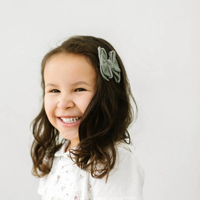 Young girl wearing a sage green Baby Bling Bows hair clip in her brown curly hair