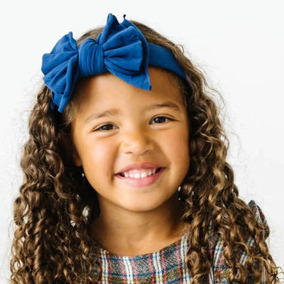 Young girl with curly hair wearing a Baby Bling Bows indigo fabric hard headband.